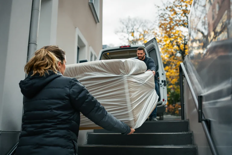 To flyttefolk bærer en indpakket sofa ud til flyttebilen, fra Adias side om SEO for flyttemænd